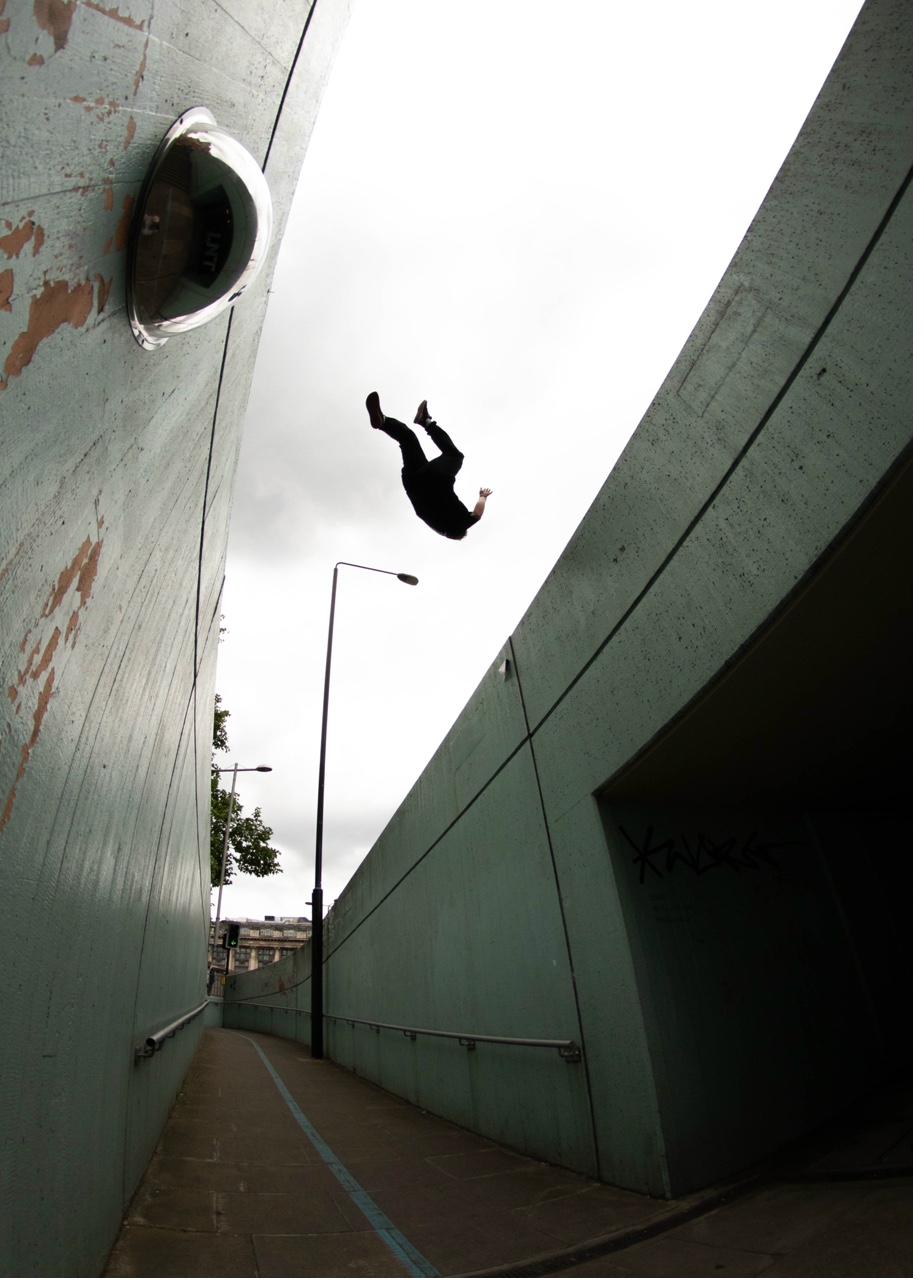 Athlete performing a backflip between concrete walls in an urban underpass